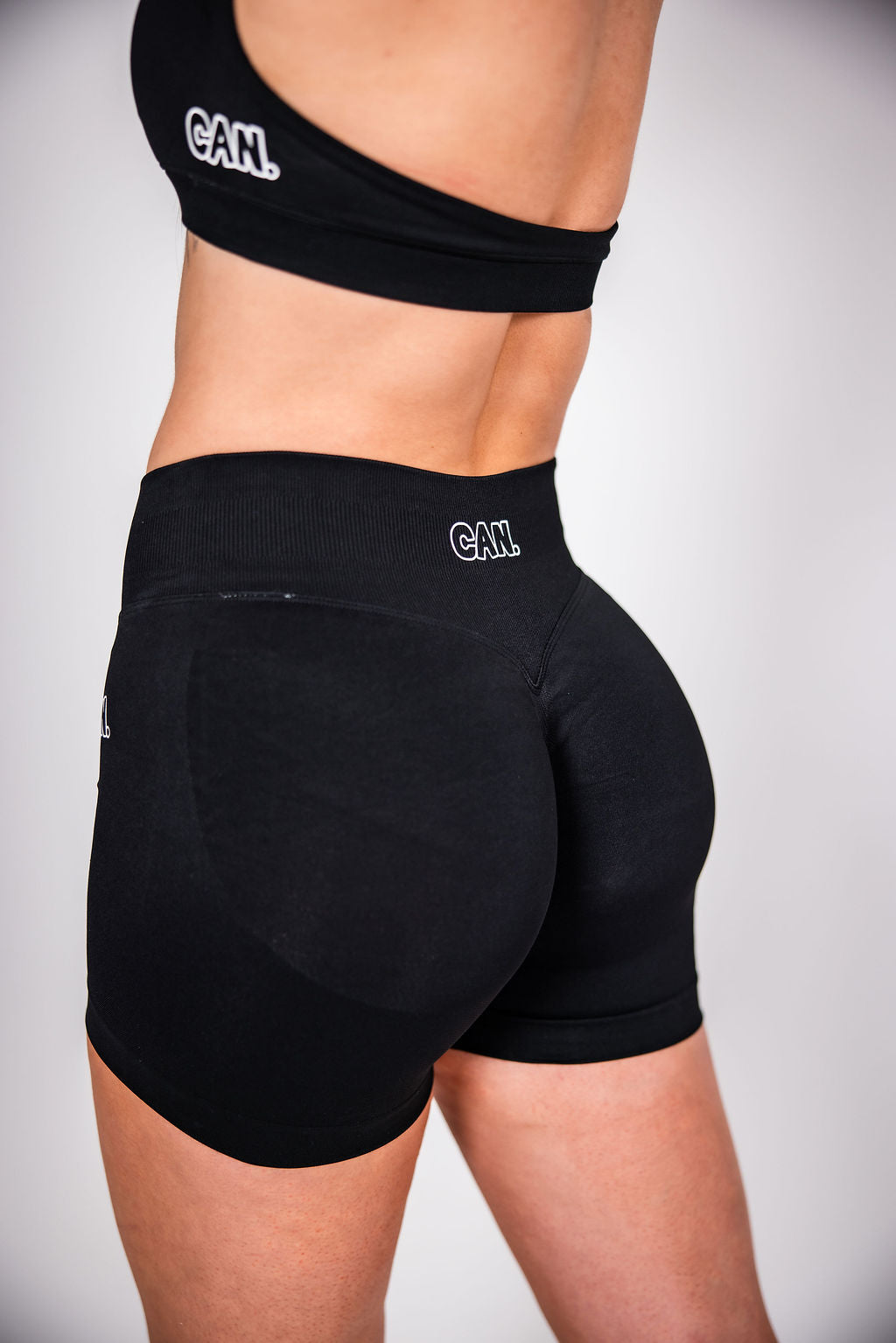 Woman wearing black CAN. Syndicate Contour Sculpt Shorts and CAN. Syndicate Contour Sculpt Crop Top on a white background. 