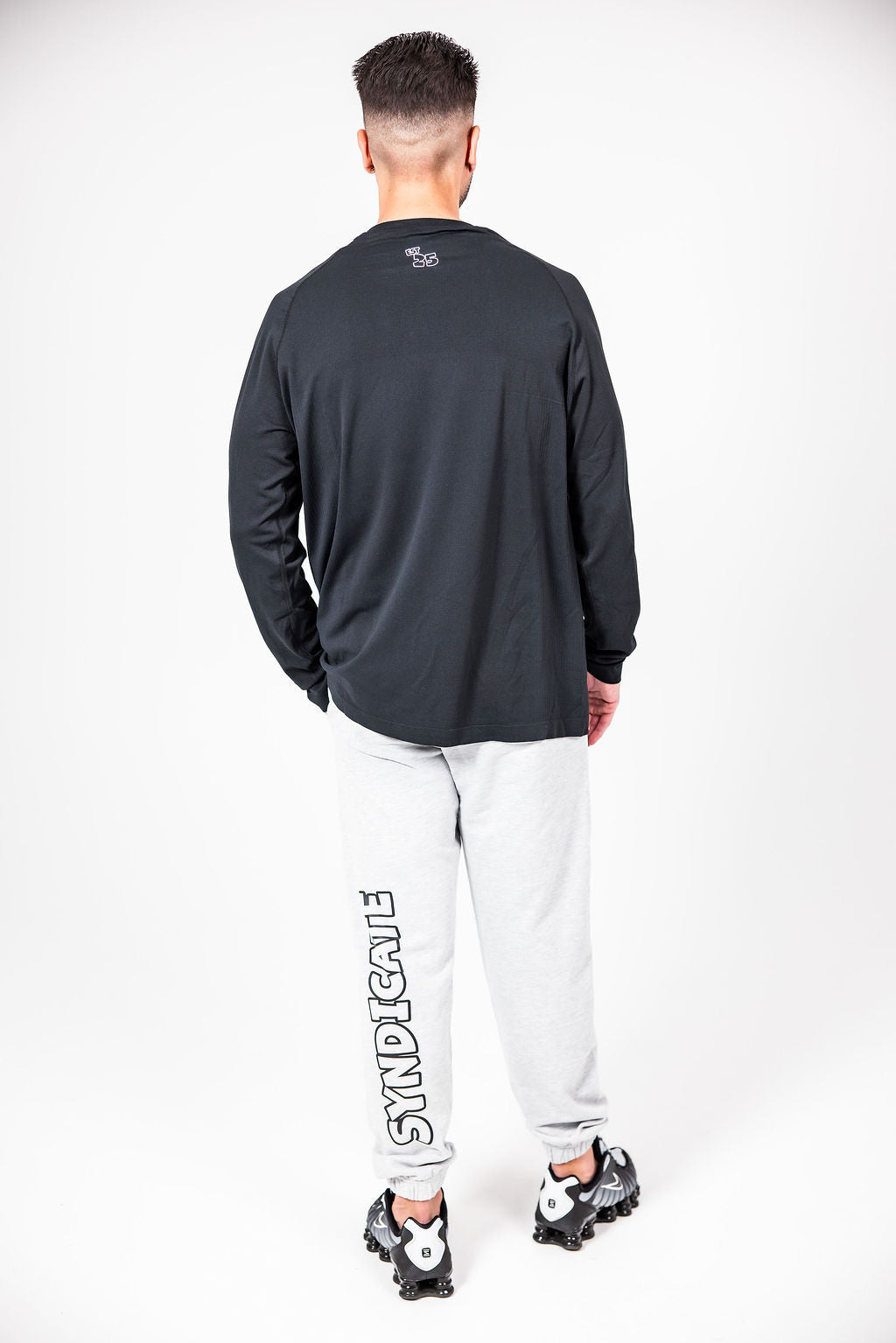 A ma wearing a CAN. Syndicate Men's Long Sleeve Athletic Tee and Grey CAN. Statement Cuffed Track Pants.