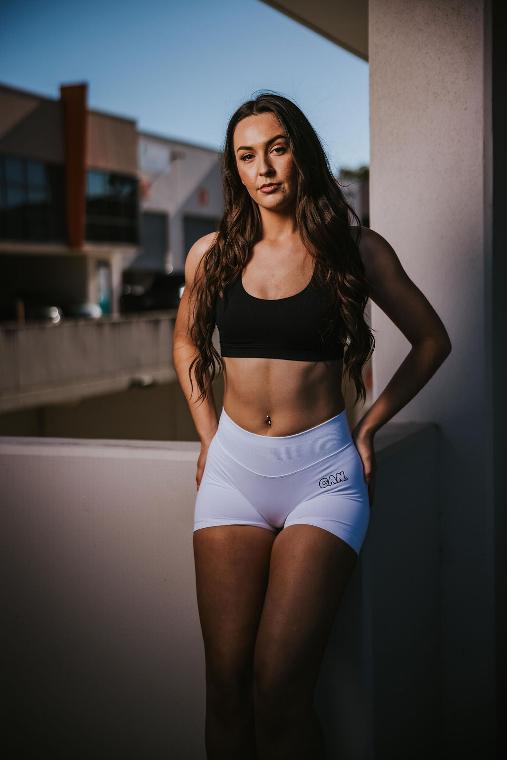 Woman with long brown hair posing in an industrial area wearing CAN. Syndicate Contour Sculpt bike shorts and CAN. Syndicate Contour Sculpt Crop Top