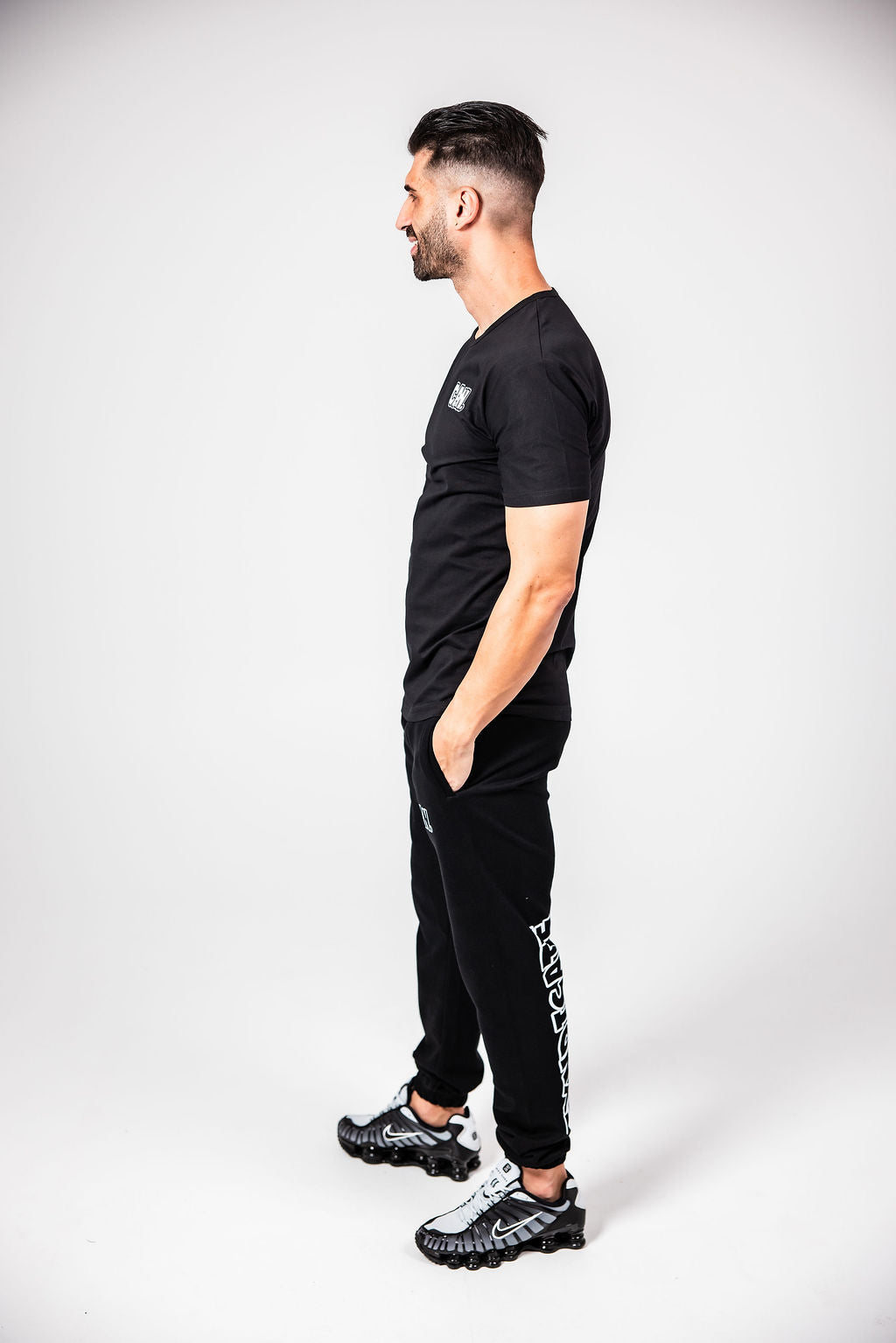 James Webb wearing a black CAN. Syndicate Men's Fitted Tee and CAN. Statement Cuffed Track Pants with 'CAN' branding on a white background