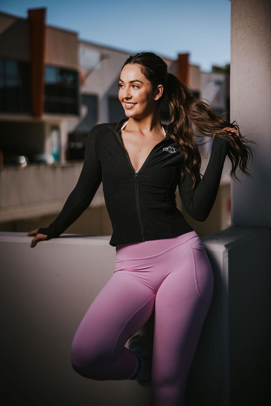 woman posing in industrial area wearing CAN. Syndicate warm up jacket and pink leggings. 