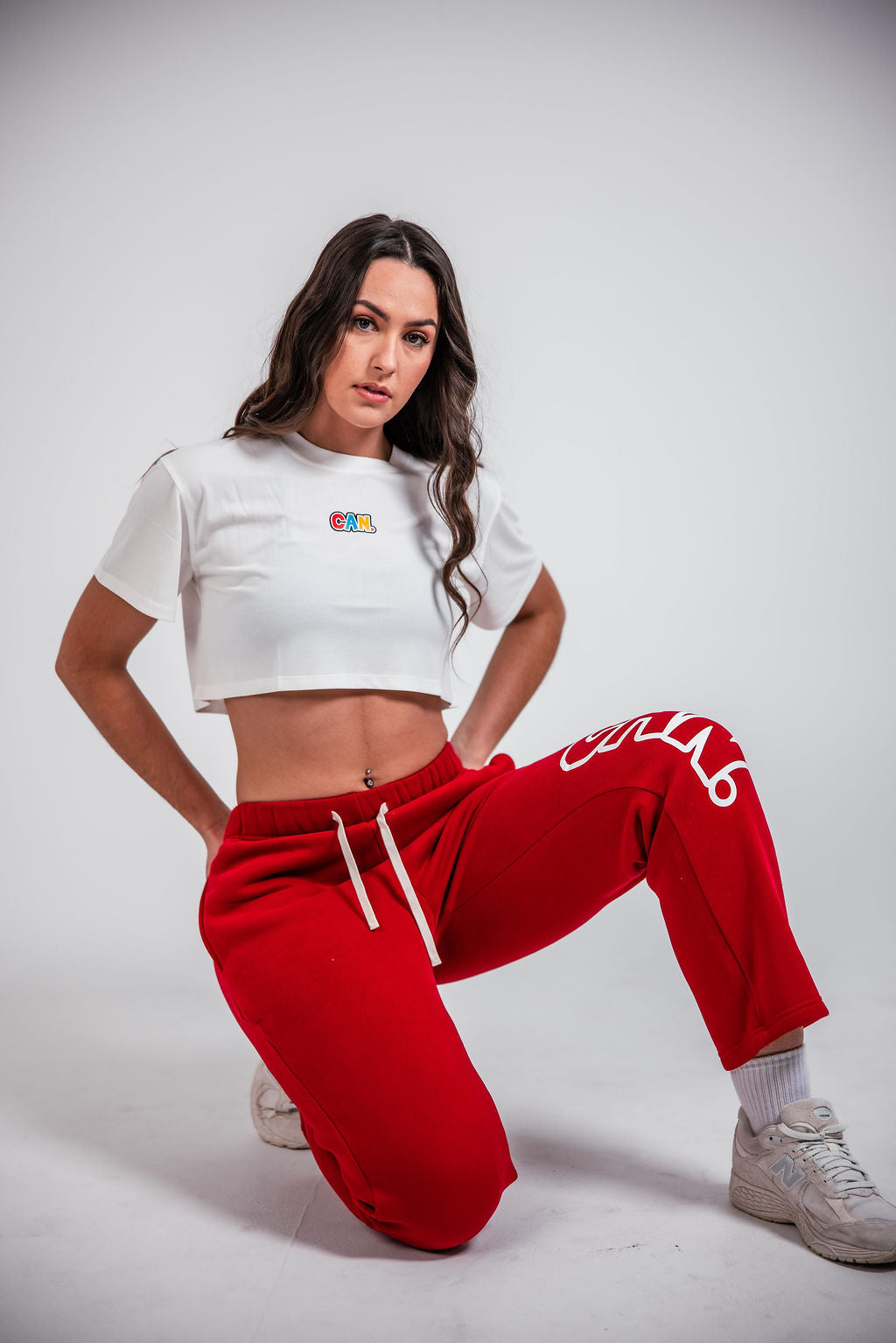a woman kneeling in front of a white background wearing a Can. Syndicate Cropped Cover Tee and red CAN. Syndicate Comfort Baggy Track Pants