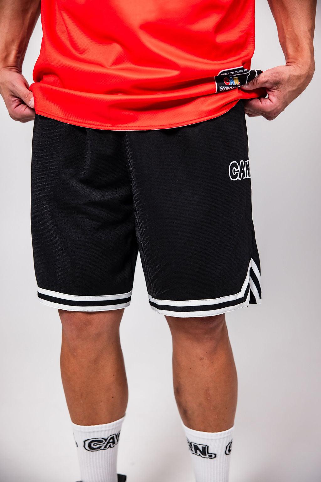 Man wearing blackCan. Syndicate Men’s Basketball Shorts and red Can. Syndicate Reversible Basketball Singlet  on white background 